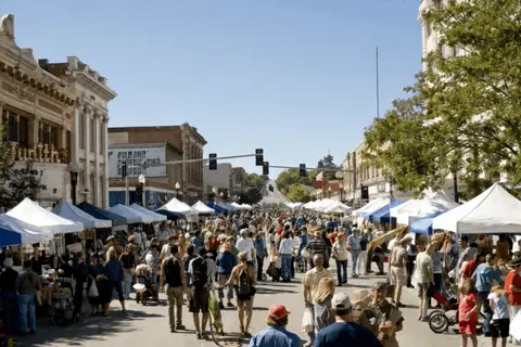 A busy street market with many vendors under white tents and crowds of people walking.