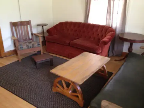 An interior view of a living room with a red sofa, a wooden armchair, and a coffee table with wagon-wheel legs.
