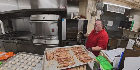 A person works in a commercial kitchen with food preparation on counters.