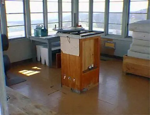 Interior view of a lookout tower with a fire finder table and surrounding windows.