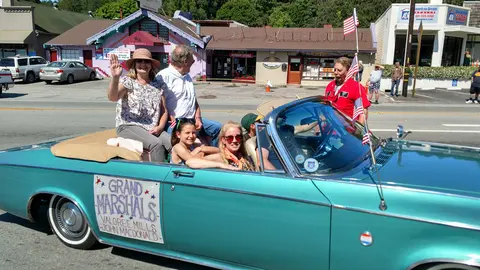 People ride in a teal convertible during a parade.