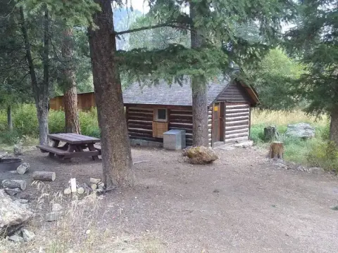 A log cabin sits among trees with a picnic table nearby.