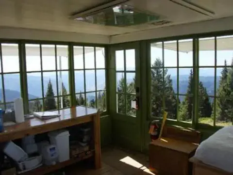 The interior of a small cabin with windows showing a mountain and forest view.