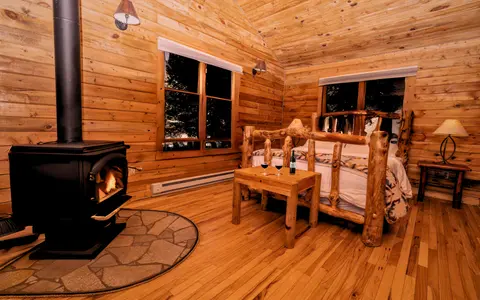 A cozy wooden bedroom featuring a wood-burning stove and rustic log bed.