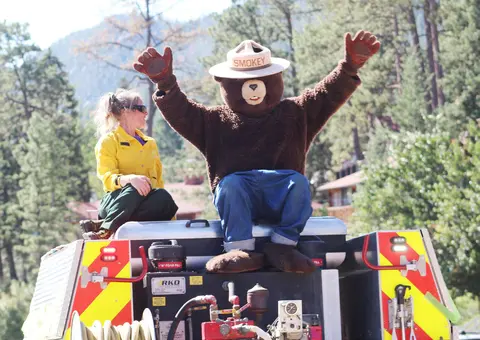A person in a bear mascot costume rides on top of a fire engine.