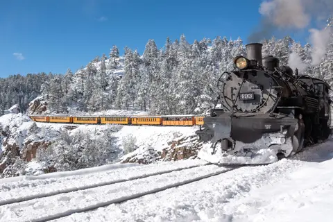 A steam train travels through a snowy mountainous landscape.