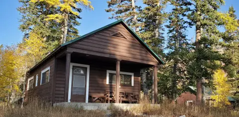 A brown wooden cabin with a covered porch surrounded by autumn trees.