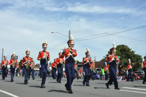 A marching band in uniform walks down a street during a parade.