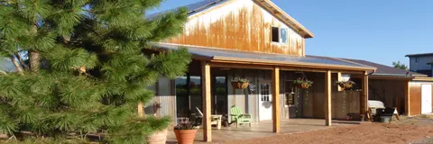 A rustic barn-style building with a covered porch and a pine tree in the foreground.