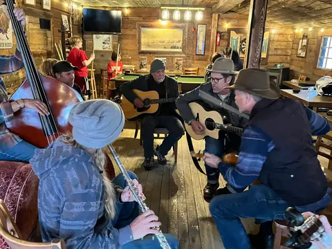 A group of people play acoustic instruments and a flute indoors.