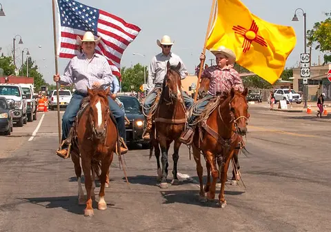 Three horsemen carry flags down a street.