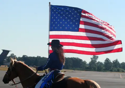 A person on a horse holds a large American flag outdoors.