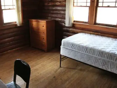 Interior view of a bedroom in a log cabin with a bed and dresser.