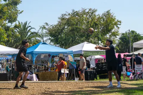 Two young men play volleyball outdoors near festival tents.