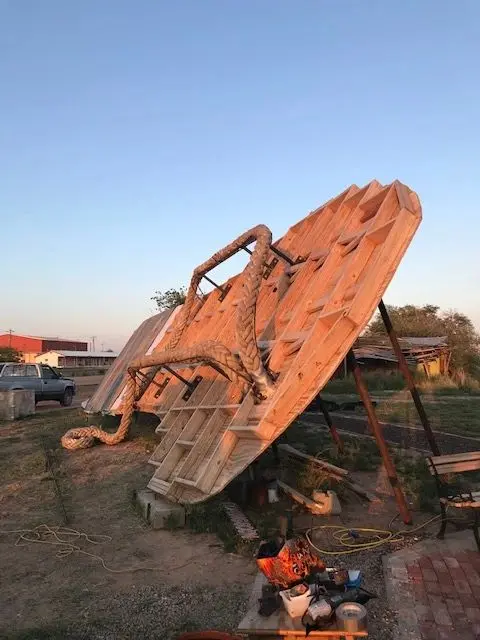 A large wooden sandal sculpture stands outdoors.