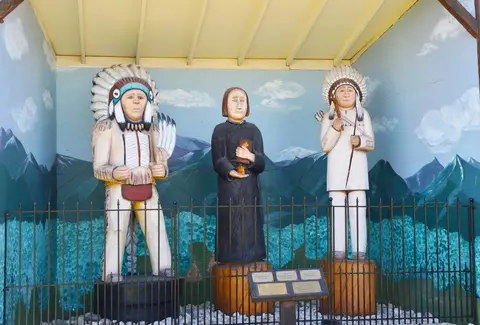Three wooden statues behind a low metal fence in front of a painted backdrop.