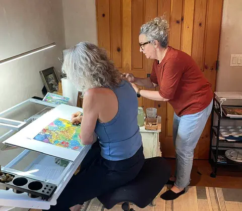 Two women working on a colorful artwork in an indoor studio setting.