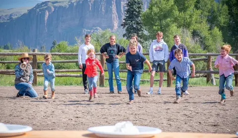 Children participate in a foot race outdoors with mountains in the background.