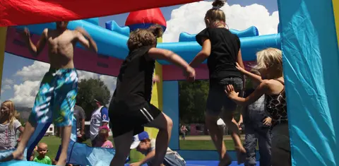 Children jump inside a colorful inflatable bounce house outdoors.