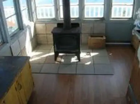 A wood-burning stove sits on a tiled hearth in a room surrounded by windows.