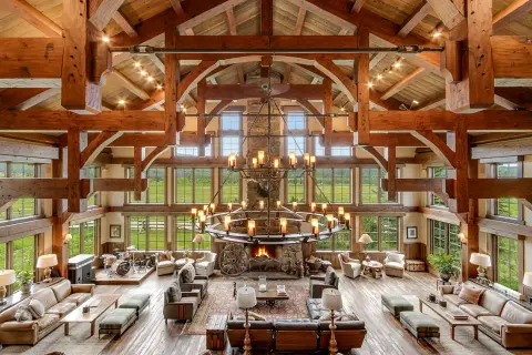 A high-angle interior view of a large rustic living room with timber framing and a massive chandelier.