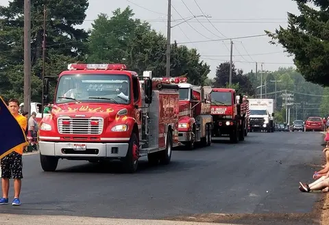 A line of red fire trucks drives down a street during a parade.