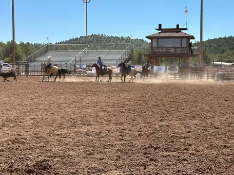 Cowboys on horseback in a dirt rodeo arena.