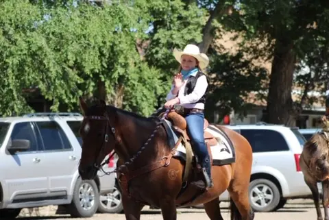 A young person in a cowboy hat rides a horse outdoors.