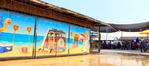 An exterior view of a building with a large beach-themed mural on the wall and water dripping from the roof.