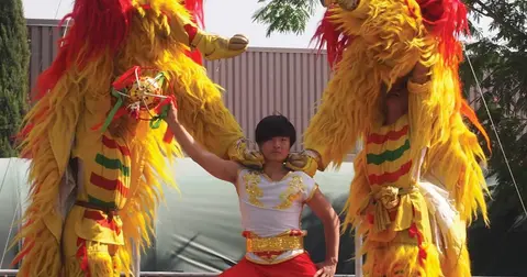 Performers in traditional lion dance costumes pose outdoors.