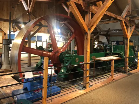 A large vintage industrial steam engine inside a wooden structure.