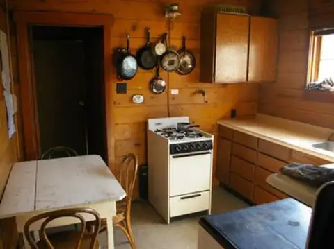 A rustic wooden kitchen with a stove, cabinets, and a dining table.