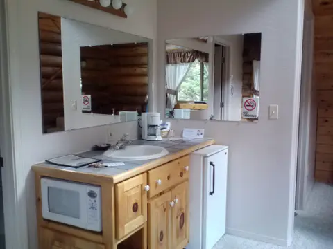 An interior view of a wooden bathroom vanity counter with a sink, microwave, coffeemaker, and mini-fridge.