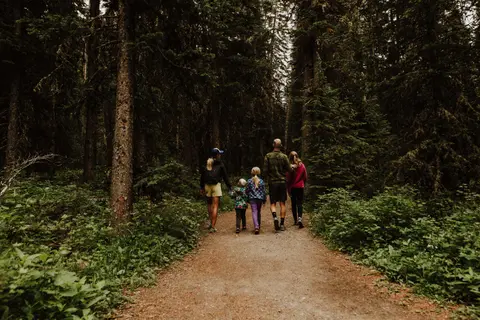 A family walks along a dirt trail through a dense forest.