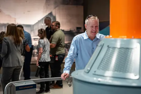 People visit an indoor exhibit featuring a generator model and historic wall graphics.