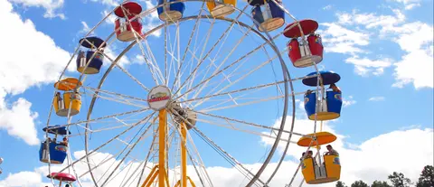 A colorful Ferris wheel stands against a partly cloudy blue sky.
