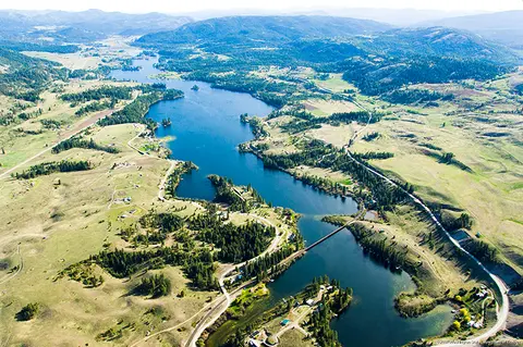 Aerial view of a long blue lake surrounded by rolling green hills and forests.