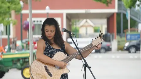 A young woman plays an acoustic guitar outdoors.