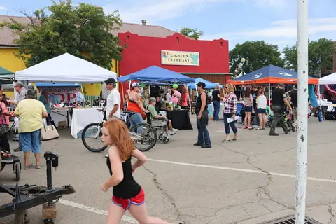 A girl runs past vendor tents and people gathered at an outdoor market.