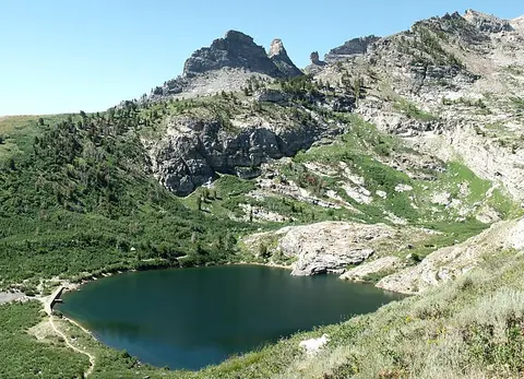 A scenic view of a mountain lake surrounded by rocky peaks and green vegetation.
