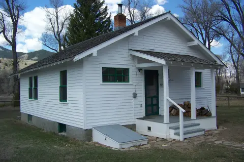 A white one-story house with green trim and a covered front porch stands outdoors.