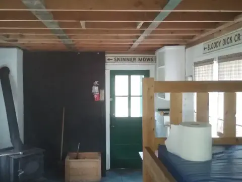 An interior view of a rustic cabin showing exposed wooden ceiling beams and a bunk bed.