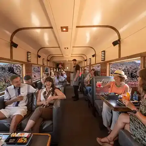 Passengers enjoy meals and drinks inside a passenger train car.