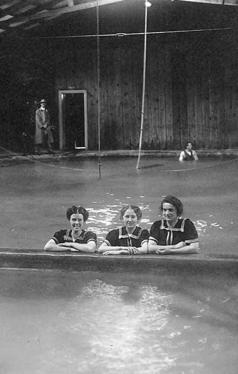 A black and white photograph of three women in an indoor pool.