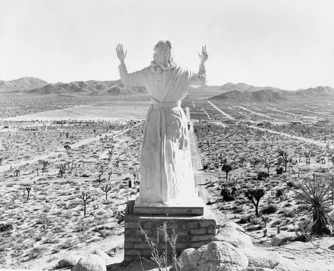 A statue overlooking a desert landscape with mountains in the background.