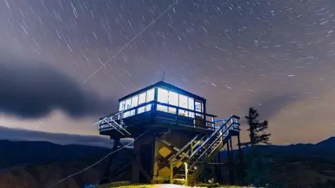 A fire lookout tower stands against a starry night sky.