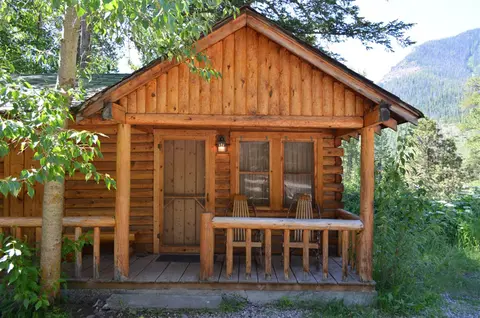 A rustic wooden cabin with a porch set against a mountain backdrop.