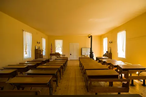 An interior shot of a historic schoolhouse classroom with wooden desks and yellow walls.