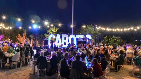 An outdoor evening gathering of people seated at tables under string lights.