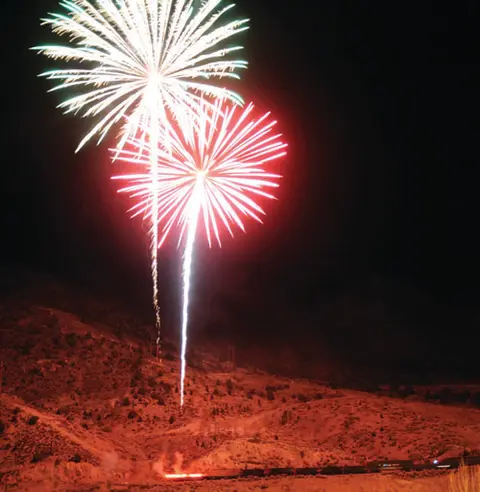 Fireworks light up the night sky over a mountainous landscape.